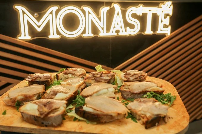Tagliere di crostoni con porchetta e rucola sotto l'insegna luminosa del Monastè