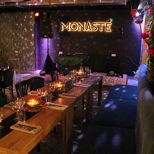 La sala del Monastè apparecchiata per un evento, con candele sui tavoli, divanetti blu e il palco sotto l'insegna luminosa