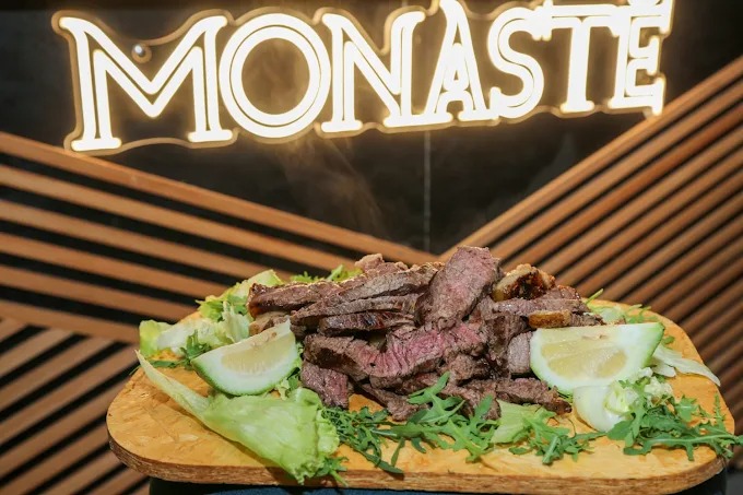 Tagliata di manzo con rucola, insalata e limone sotto l'insegna luminosa del Monastè